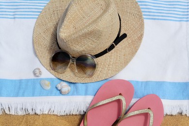 Beach towel with straw hat, seashells, sunglasses and flip flops on sand, flat lay