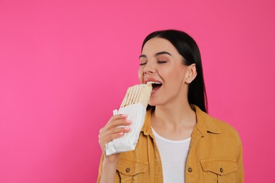Young woman eating delicious shawarma on pink background. Space for text