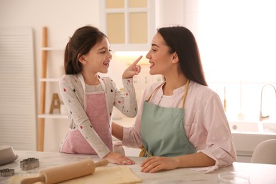 Mother with her cute little daughter having fun while rolling dough in kitchen