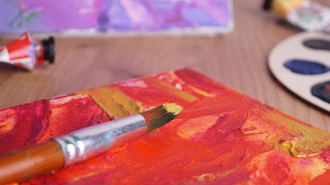 Photo of Artist's canvas with mixed paints and brush on wooden table, closeup