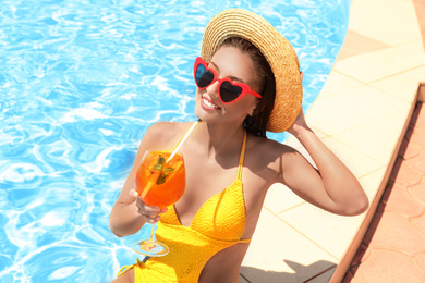 Woman with glass of refreshing drink near swimming pool