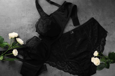 Elegant black plus size women's underwear and beautiful roses on grey background, flat lay