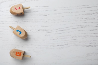 Hanukkah traditional dreidels with letters Nun, Gimel and Shin on white wooden background, flat lay. Space for text
