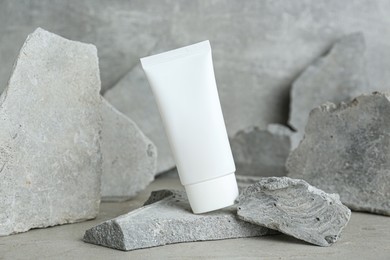 Tube of hand cream among stones on grey background. Mockup for design