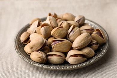 Plate with pistachio nuts on beige tablecloth, closeup