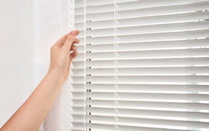 Woman opening white horizontal window blinds, closeup