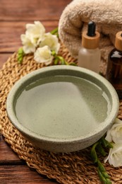 Photo of Bowl of essential oil and beautiful flowers on wooden table. Aromatherapy treatment