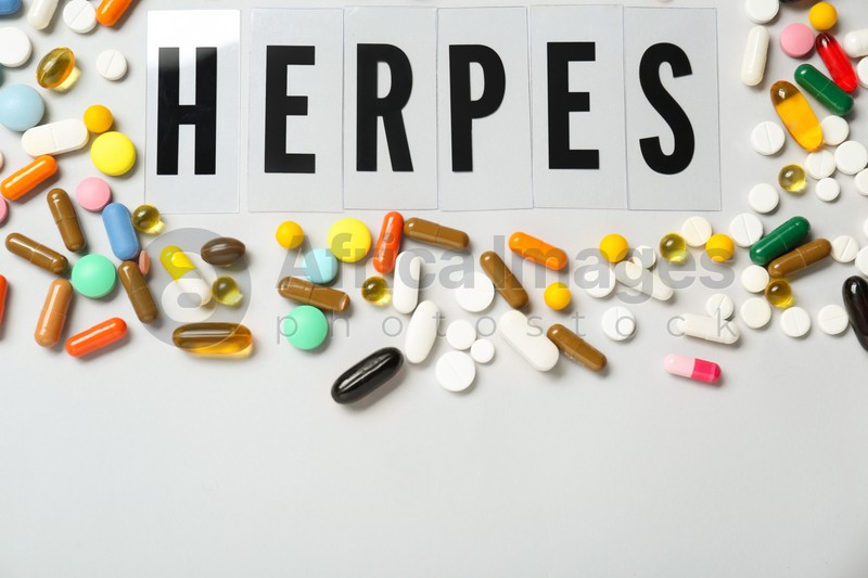 Word Herpes surrounded by different pills on white background, top view. Space for text