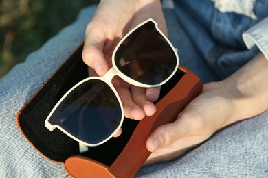 Woman holding sunglasses in brown leather case outdoors on sunny day, above view