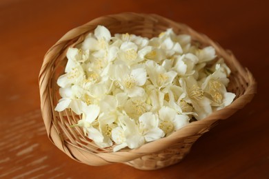 Beautiful white jasmine flowers in wicker basket on wooden table, closeup