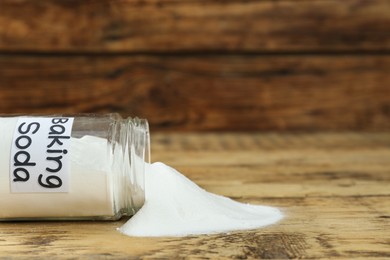 Overturned jar with baking soda on wooden table, closeup. Space for text