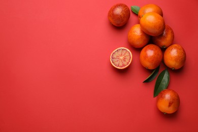 Many ripe sicilian oranges and leaves on red background, flat lay. Space for text