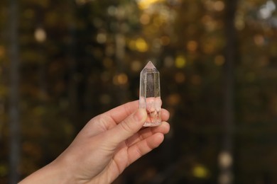 Woman holding clear quartz crystal outdoors, closeup
