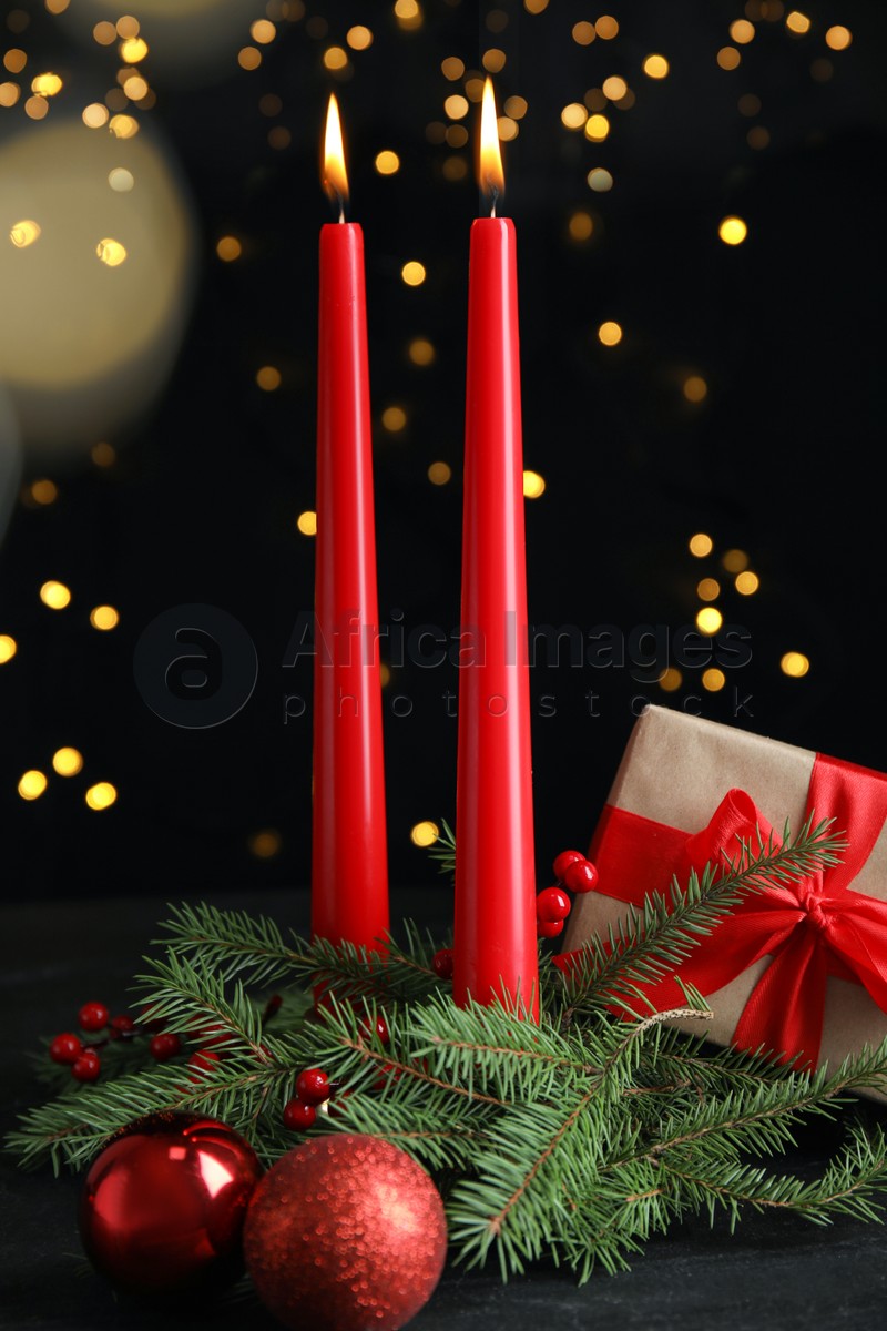 Photo of Burning candles, gift box and decor on dark table against blurred festive lights. Christmas eve