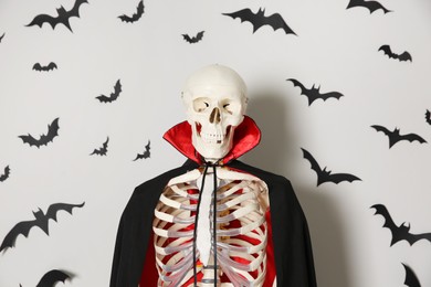 Skeleton in cloak and paper bats on light wall
