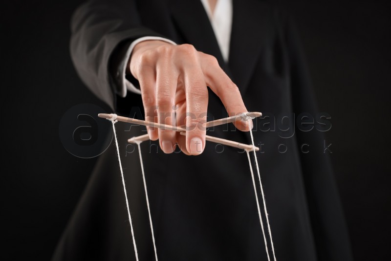 Photo of Woman in suit pulling strings of puppet on black background, closeup