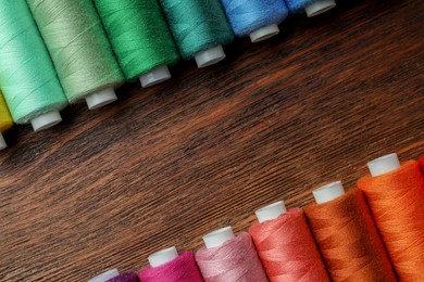 Frame of colorful sewing threads on wooden table, flat lay. Space for text