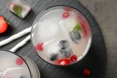 Glasses of refreshing drink with ice cubes and berries on grey table, top view