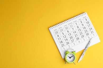 Calendar, pen and alarm clock on yellow background, flat lay. Space for text