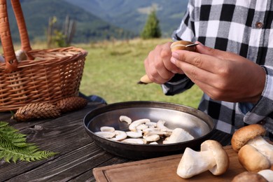 Man slicing mushrooms at wooden table outdoors, closeup