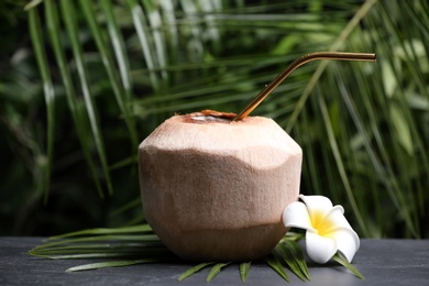 Young peeled coconut with straw and flower on black table