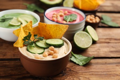 Bowl of delicious classic hummus with tortilla chips, cucumber and parsley on wooden table. Space for text
