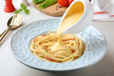Photo of Pouring tasty cheese sauce onto spaghetti with meat on light grey table, closeup