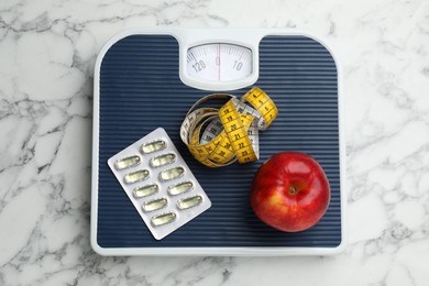 Scales with oil capsules, apple and measuring tape on white marble table, top view. Weight loss