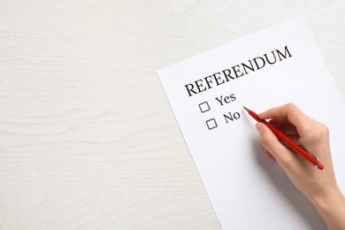 Woman with referendum ballot making decision at white wooden table, closeup. Space for text