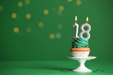 Coming of age party - 18th birthday. Delicious cupcake with number shaped candles on green background, space for text
