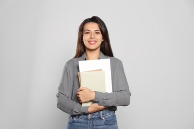 Happy young teacher with books on light grey background