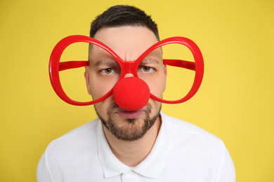 Man with clown nose and funny glasses on yellow background. April fool's day
