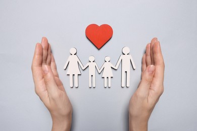 Woman protecting figures of family and heart on light background, top view. Insurance concept