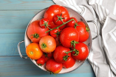 Many different ripe tomatoes in colander on light blue wooden table, top view