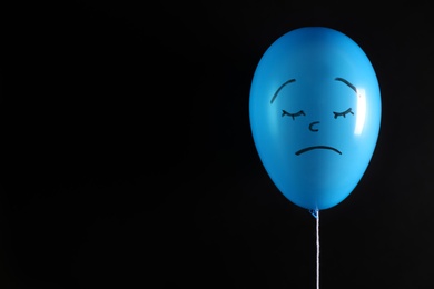 Air balloon with drawn sad face on black background. Space for text