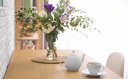 Teapot, cup and flowers on wooden dining table indoors. Kitchen interior