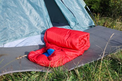 Red sleeping bag near camping tent on green grass outdoors