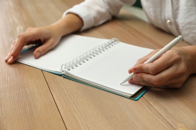 Left-handed woman writing in notebook at wooden table, closeup