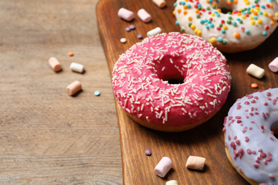 Yummy donuts with sprinkles and marshmallows on wooden table, closeup