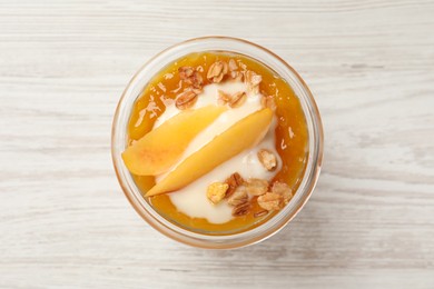 Tasty peach yogurt with granola, jam and pieces of fruit in glass on white wooden table, top view