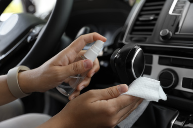 Woman cleaning gear stick with wet wipe and antibacterial spray in car, closeup