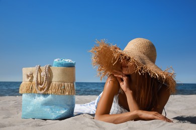 Woman with beach bag and straw hat lying on sand near sea
