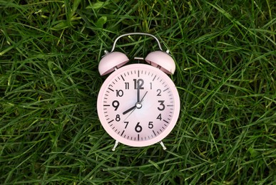 Photo of Pink small alarm clock on green grass outdoors, top view