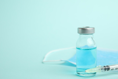 Vial, syringe and surgical mask on turquoise background, space for text. Vaccination and immunization