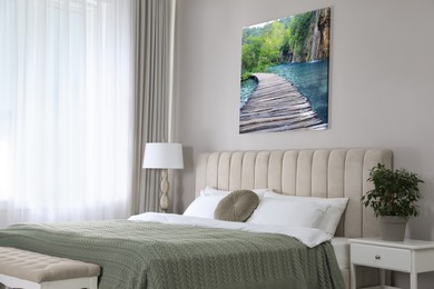 Canvas with printed photo of wooden bridge over lake and waterfall on beige wall in bedroom
