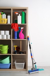 Shelving unit with detergents, cleaning tools and toilet paper near white wall indoors
