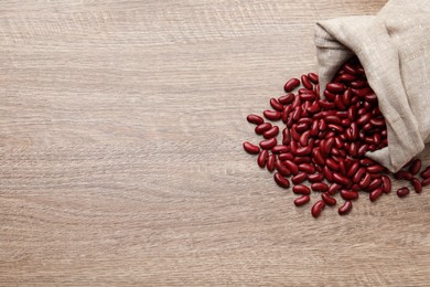 Raw red kidney beans with sackcloth bag on wooden table, flat lay. Space for text