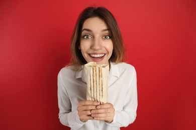 Photo of Emotional young woman with delicious shawarma on red background