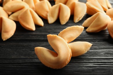 Tasty fortune cookies with predictions on black wooden table, closeup