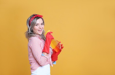 Beautiful young woman with bottle of detergent singing on orange background. Space for text